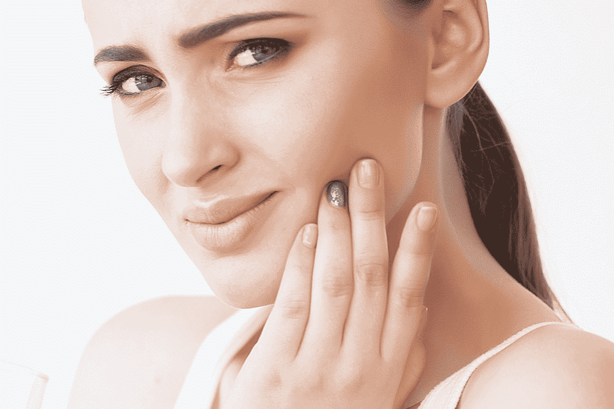 Woman touching her cheek while considering natural toothache relief options.