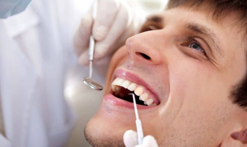 Patient receiving dental examination with mirror and suction tools during checkup.