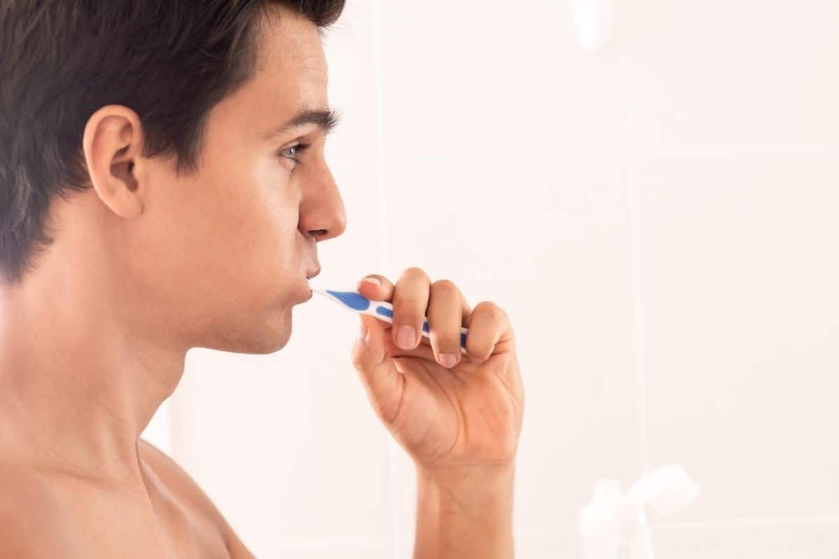 Man brushing teeth with blue toothbrush showing proper dental hygiene technique.