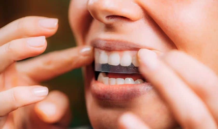 Person applying teeth whitening strip to upper teeth to demonstrate whitening effectiveness.