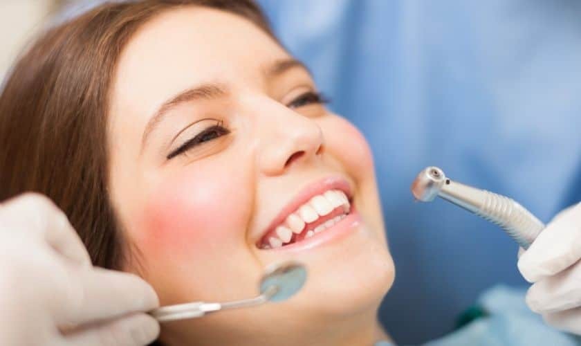 Smiling patient receiving dental treatment with high-speed drill during root canal procedure.