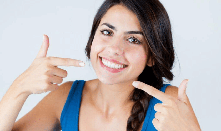 Young woman pointing to her bright white smile, promoting professional teeth whitening results.