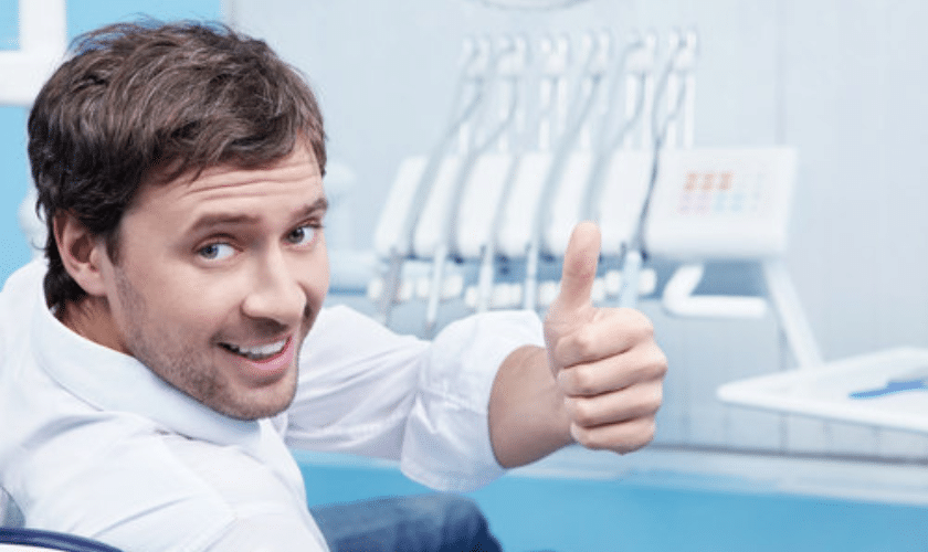 Smiling male patient giving thumbs up in a modern dental office treatment room.