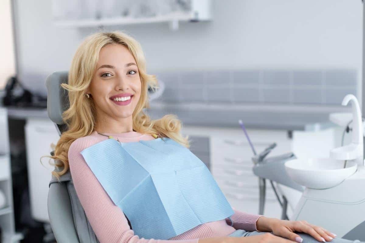 Smiling patient wearing protective bib in modern dental office treatment room.