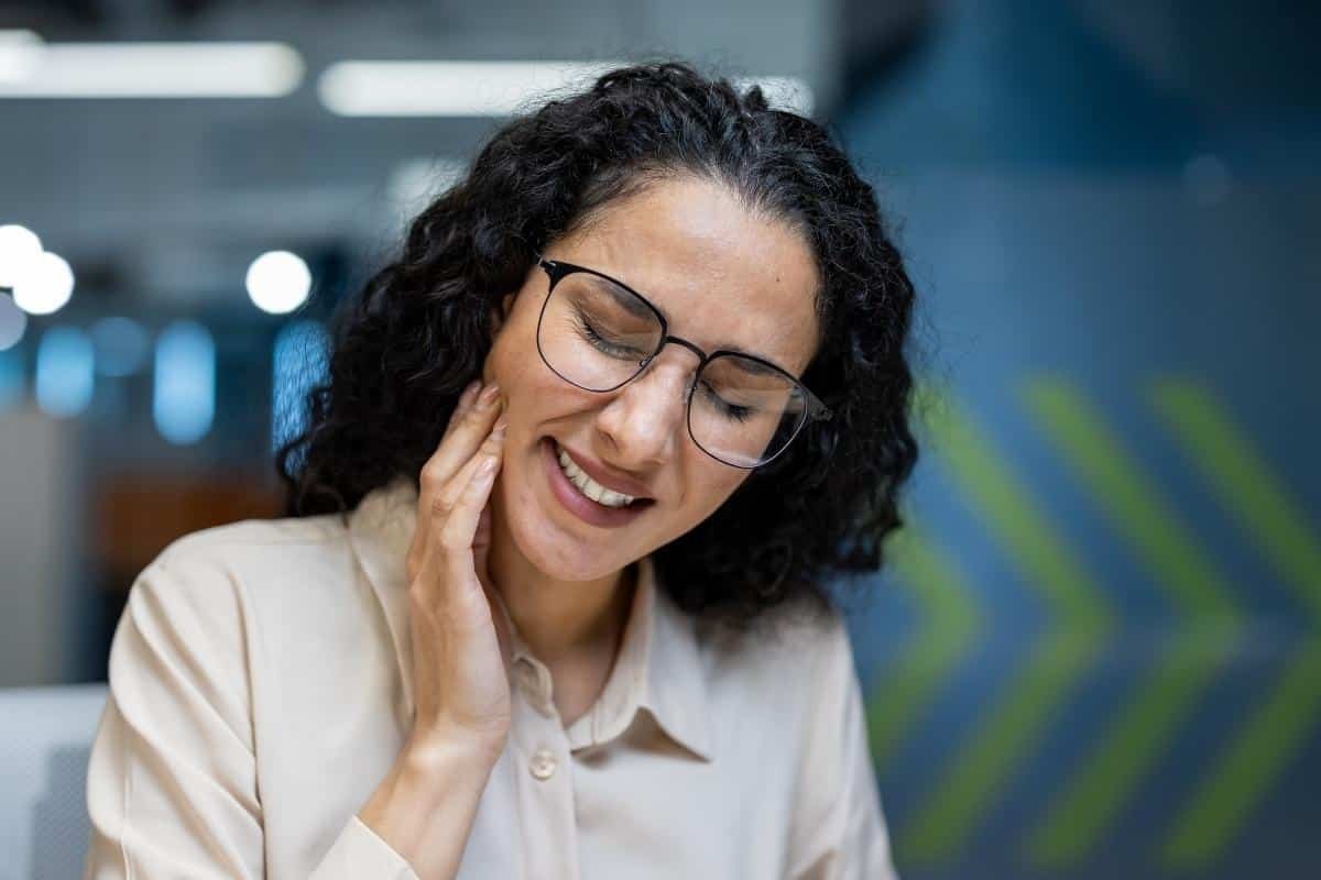 Woman with glasses smiling, touching her face in a dental office setting.
