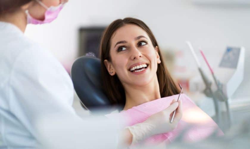 Patient smiling in dental chair during porcelain veneer consultation with dentist.