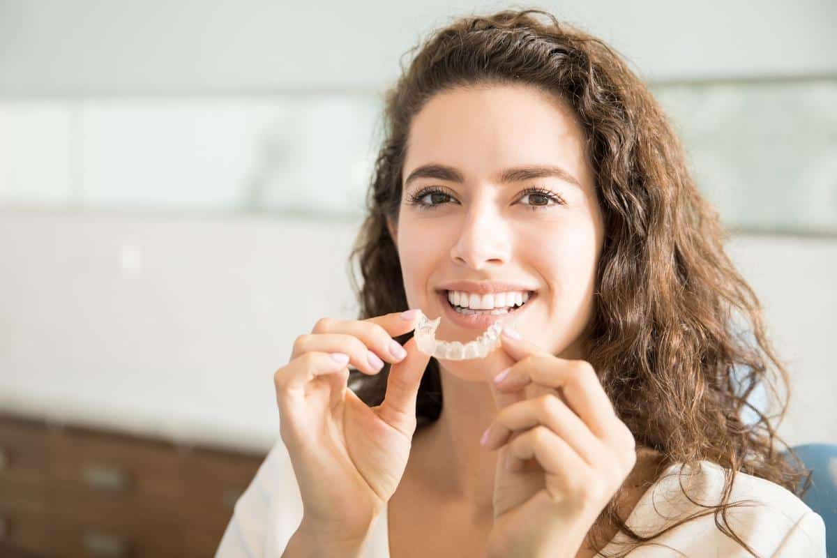 Woman flossing teeth in bright bathroom setting, smiling at camera during daily dental care routine.