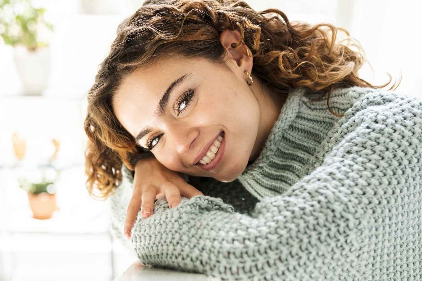 Happy woman in cozy sweater smiling after cosmetic dental care in Tempe.