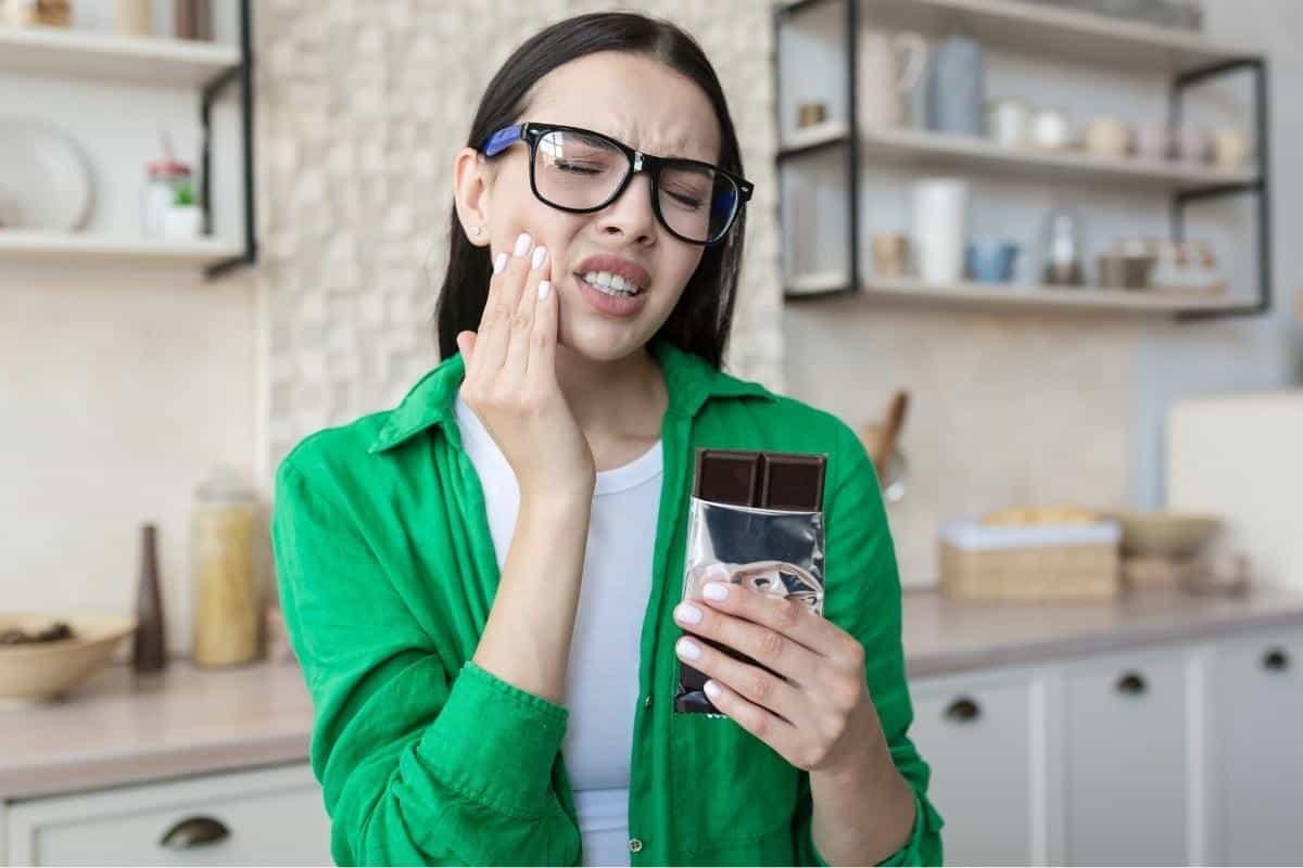 Woman in green jacket holding smartphone in modern kitchen, smiling at camera.