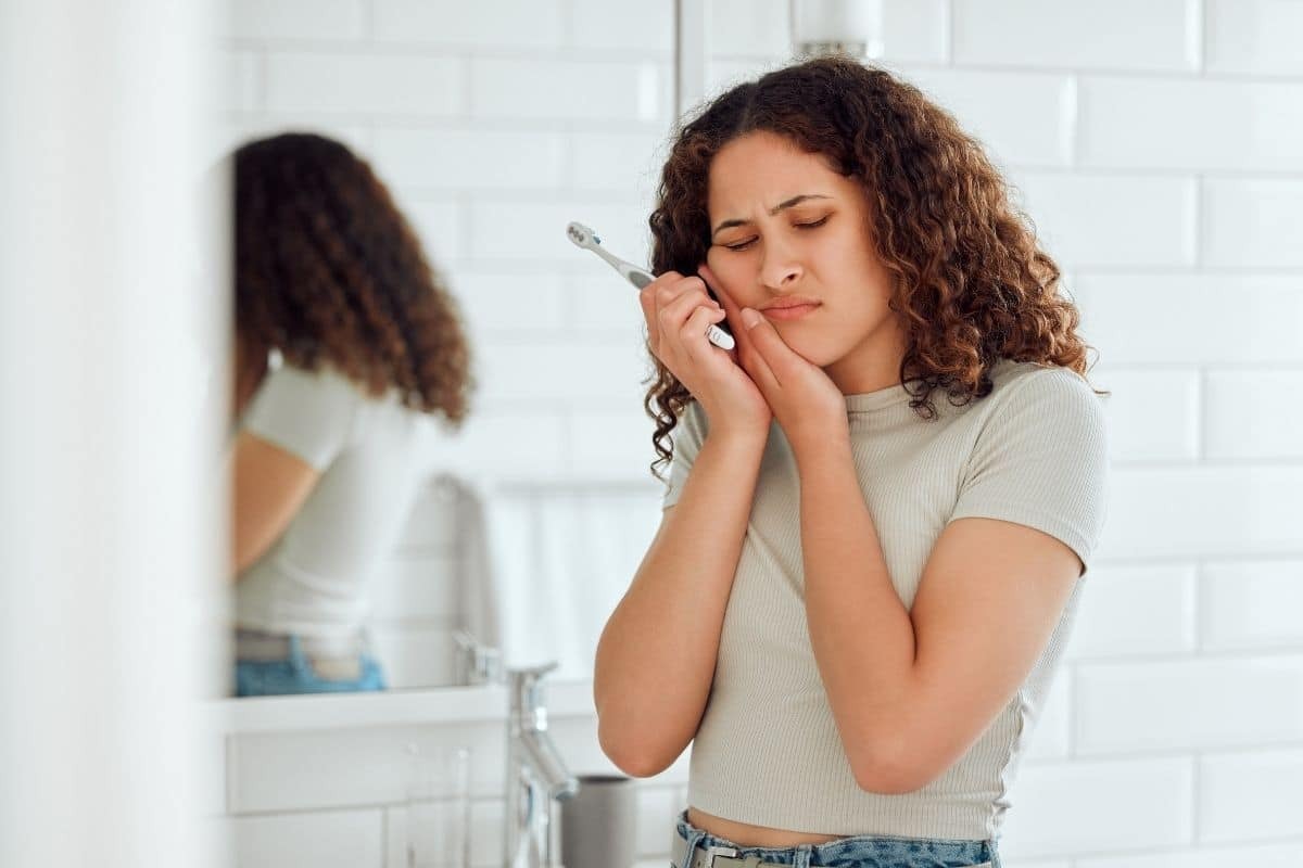 Woman examining her teeth in a bathroom mirror, checking for signs of dental problems.