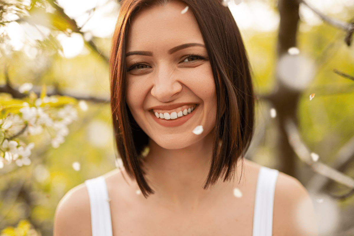 Smiling woman with bright white teeth among spring blossoms after professional teeth whitening.