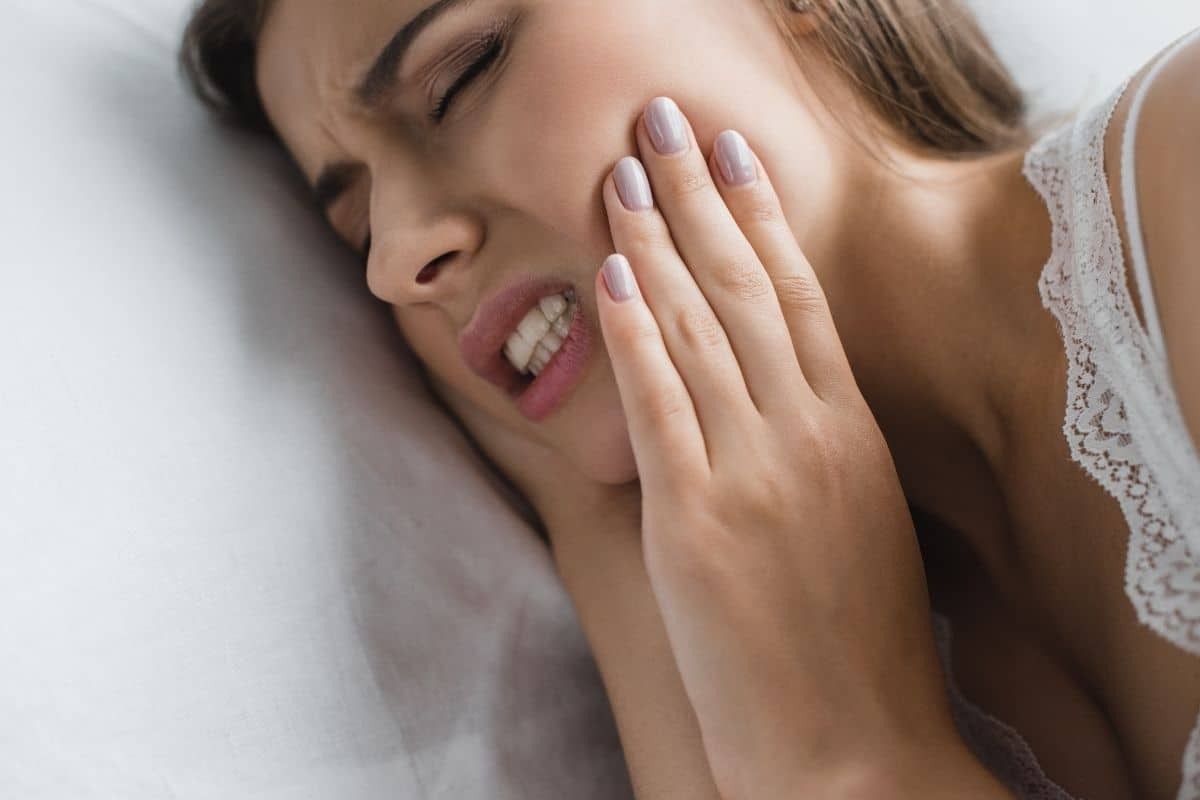 Woman holding her cheek in pain, experiencing nighttime tooth pain or dental discomfort.