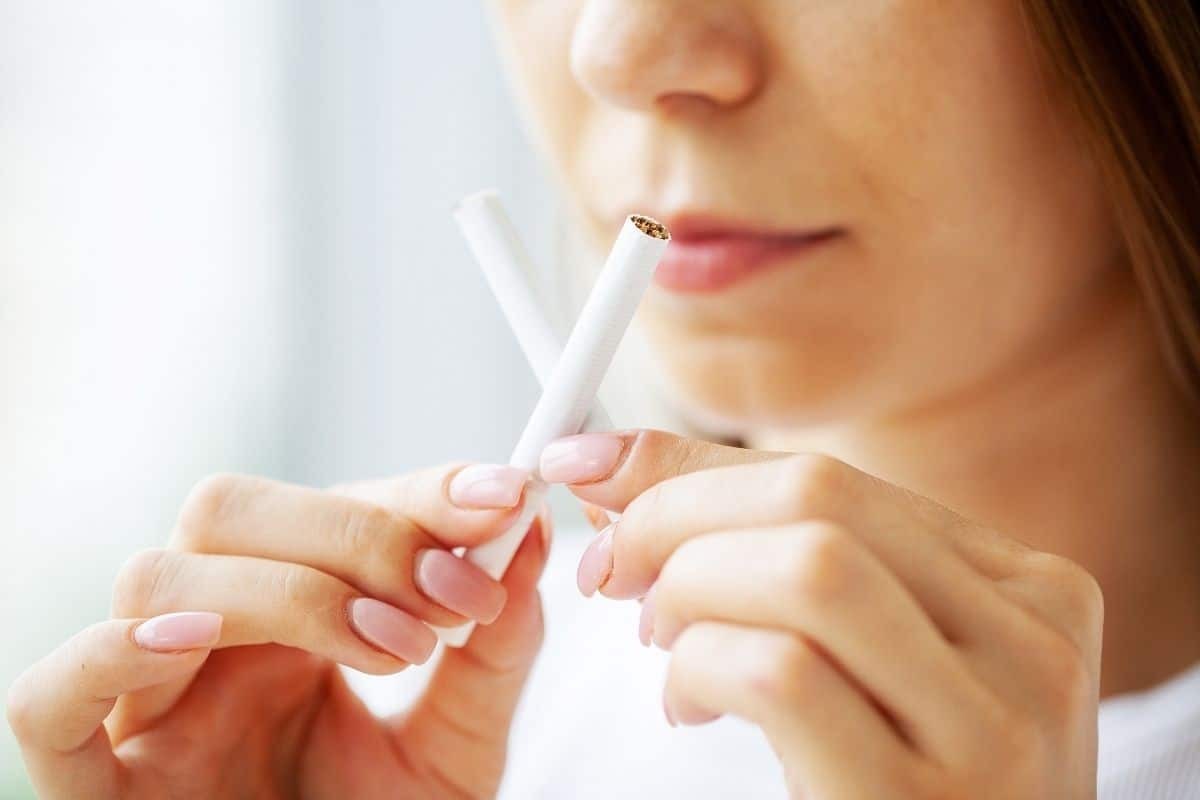 Woman breaking a cigarette in half to quit smoking and improve her oral health.