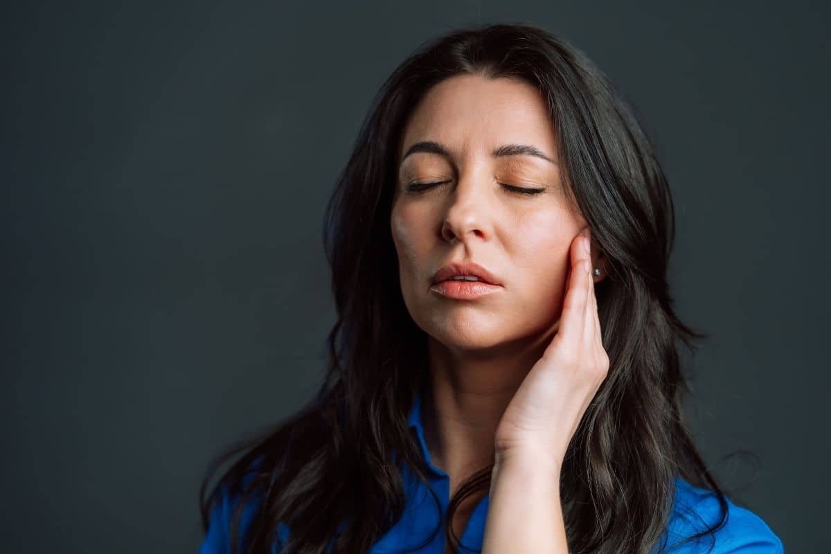 Woman with closed eyes touching her cheek, experiencing tooth pain radiating to the ear area.