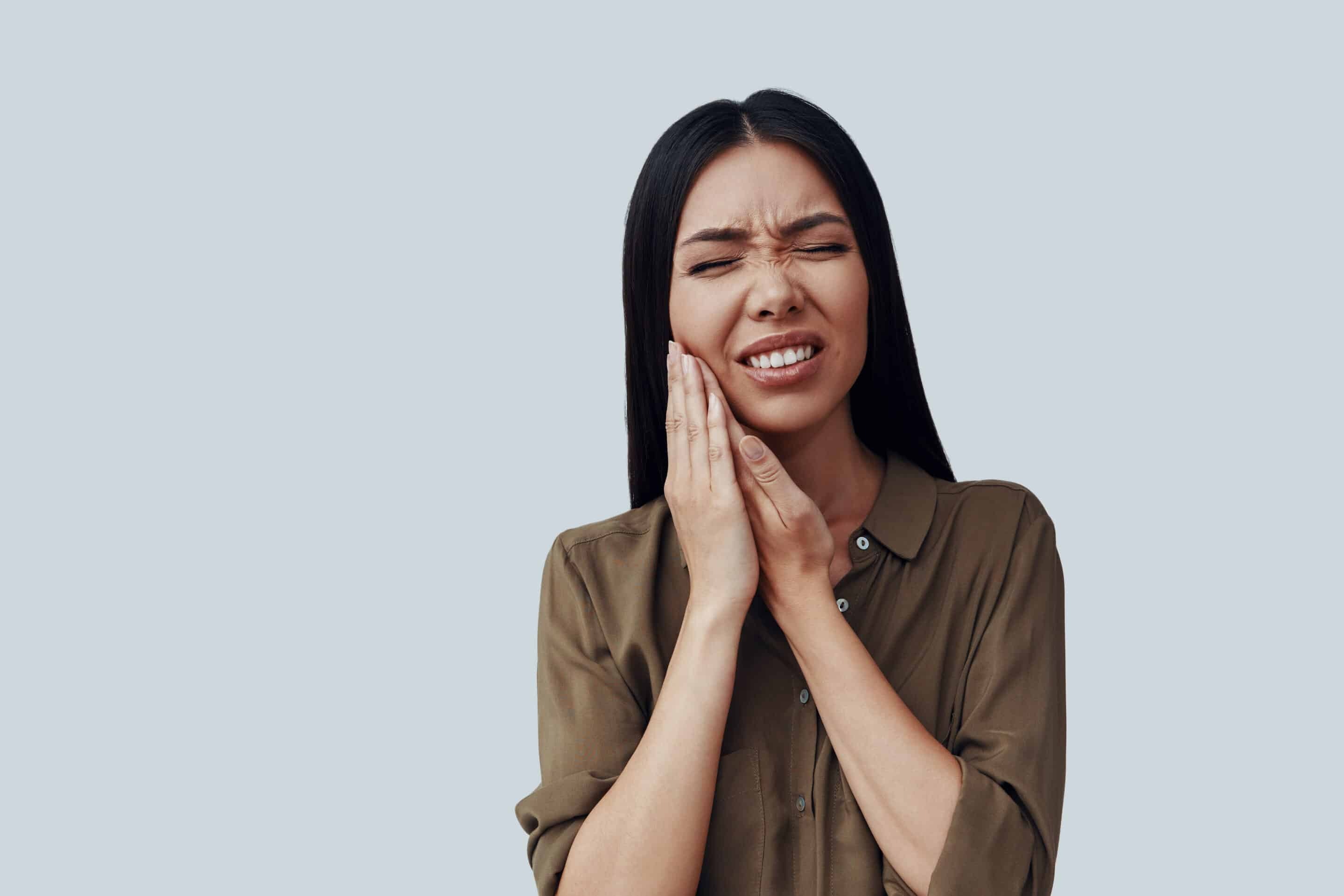 Woman experiencing tooth pain, holding her cheek in discomfort during emergency dental situation.