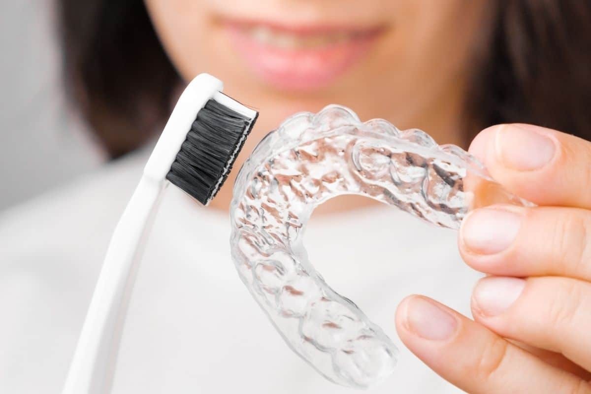 Woman holding clear Invisalign tray with toothbrush for cleaning and maintenance.