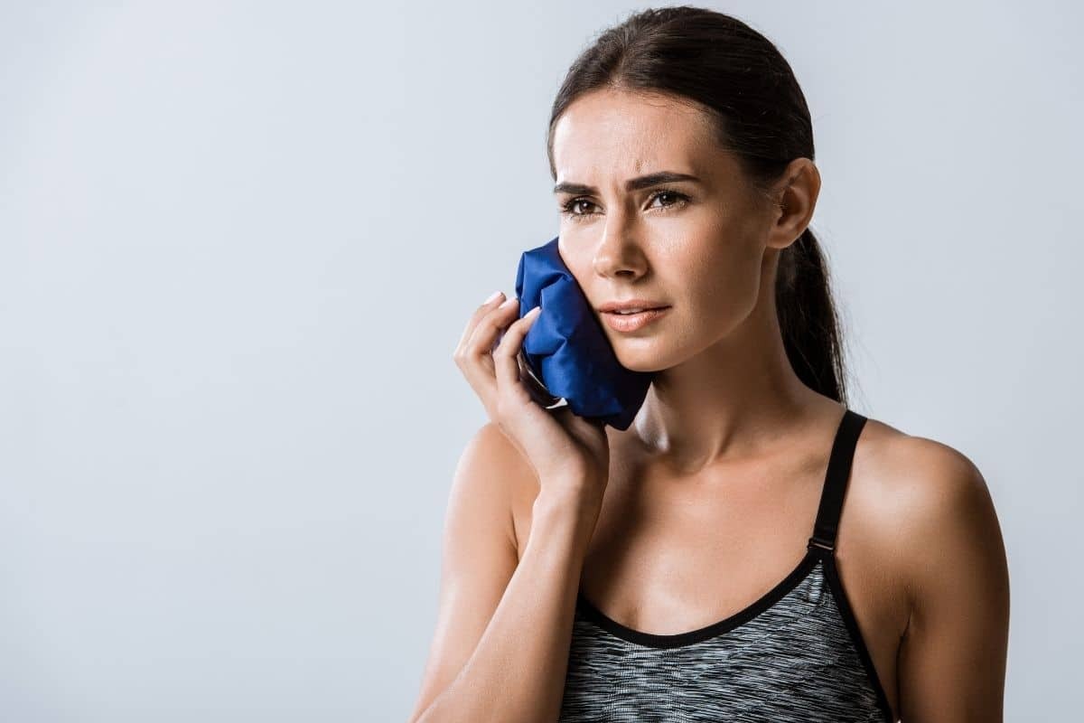 Woman with swollen gums applying ice pack to cheek for pain relief.